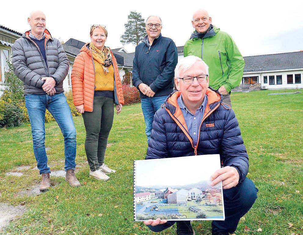 Foto der en mann sitter på huk med en illustrasjon i hendene,, og fire personer står bak 