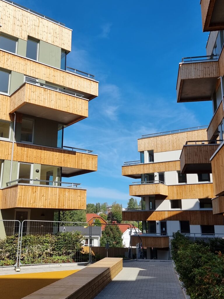 Boligbygg i 3-4 etasjer, balkonger med trebekledning, blå himmel