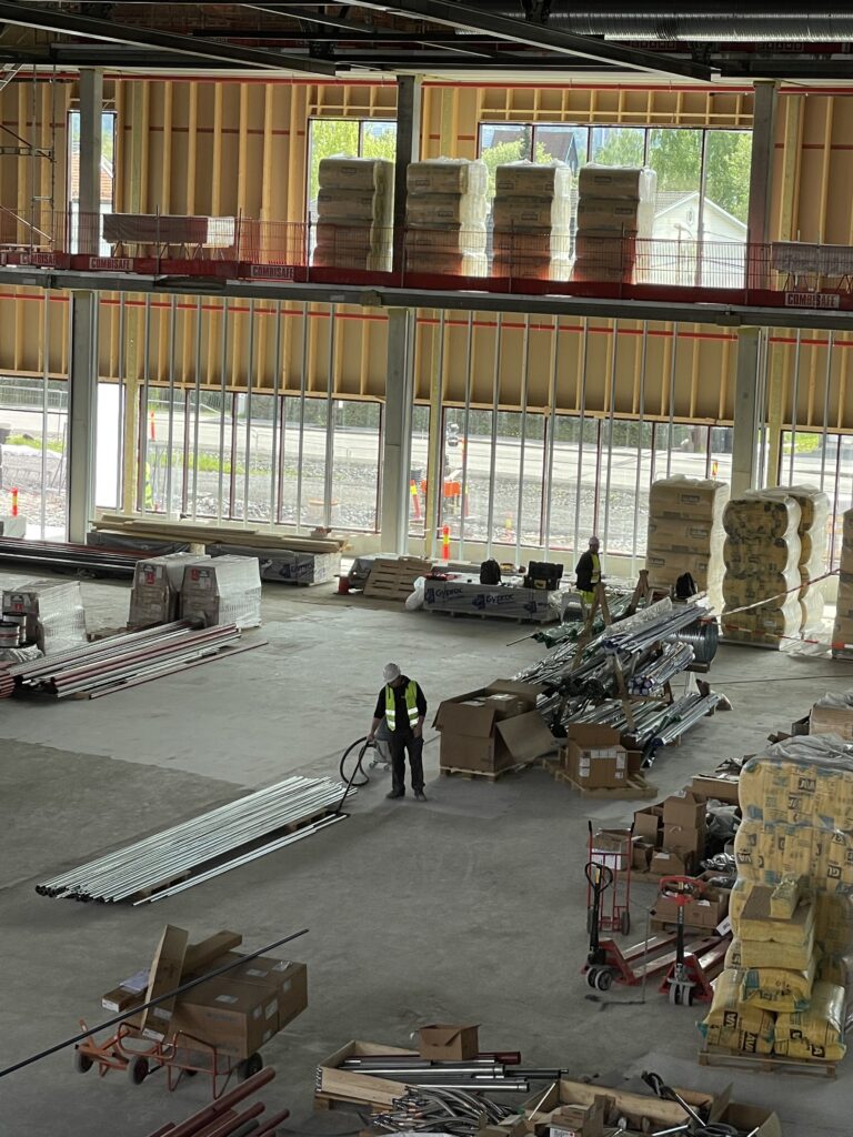 Stor, innendørs hall, byggeplass, paller med materialer, store vinduer, mann med støvsuger