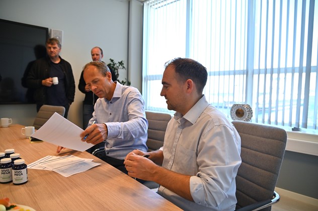 To menn i blå skjorter signerer papirer, møterom