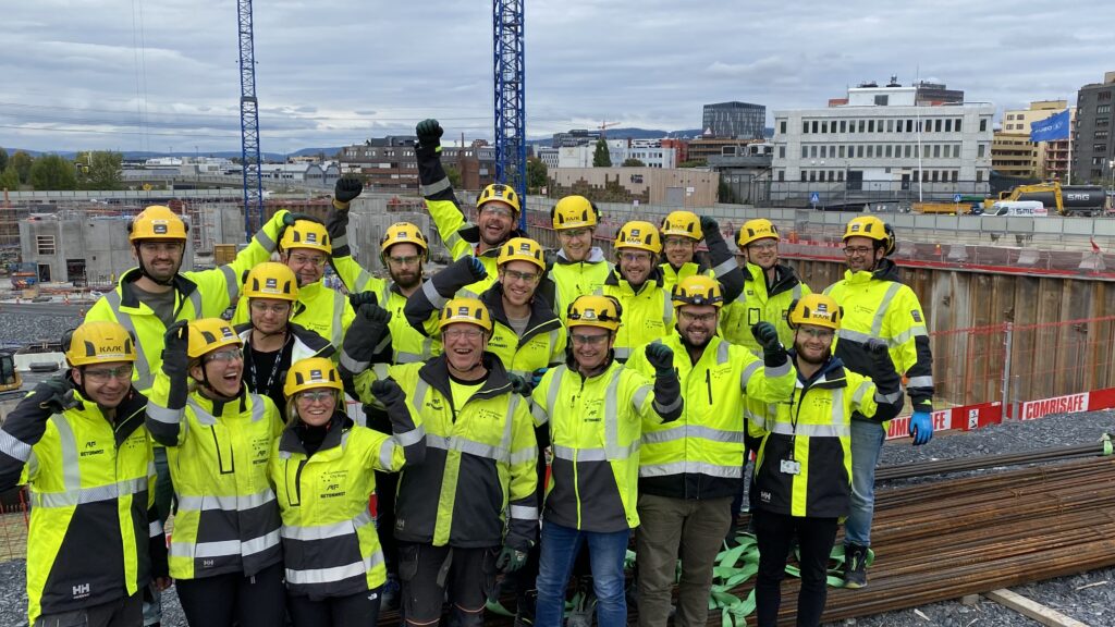 Flere kvinner og menn i verneutstyr foran byggeplass
