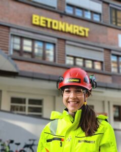 Foto, ung kvinne, verneutstyr, rød hjelm, smil, Betonmast-skilt