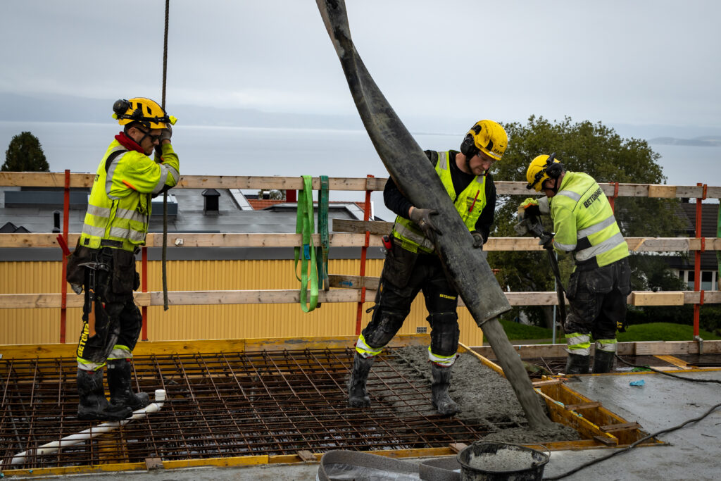 Menn i verneutstyr, utenførs, armerings, betongstøp, byggeplass, grå himmel